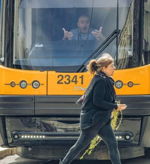 Снимката на забързана жена с върбови клонки пред потеглящ трамвай