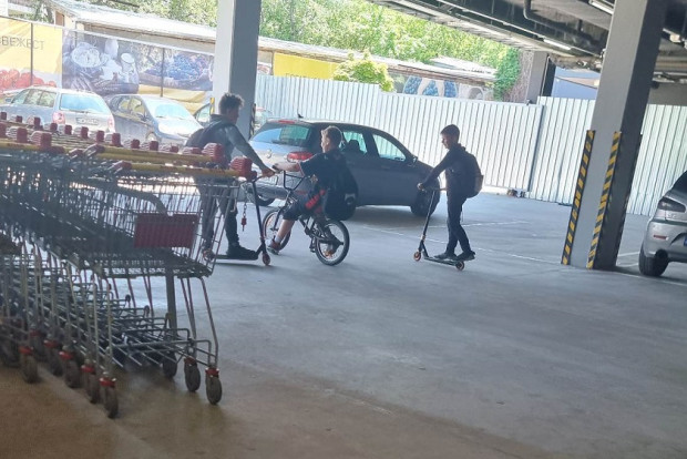 Деца хвърчат с колела и тротинетки на паркинг на хипермаркет
